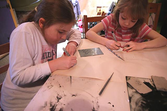 Two children sitting at a table drawing on zinc plates with sharpie pens.