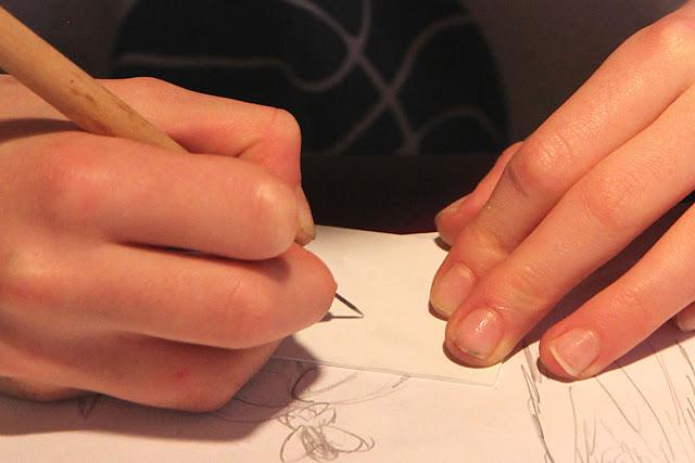An image of a pair of hands scratching into a white plastic plate with a metal scribe.