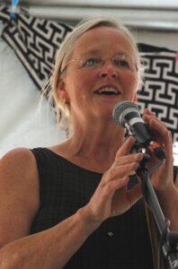 A woman standing singing at a microphone, with a beautiful open smile!