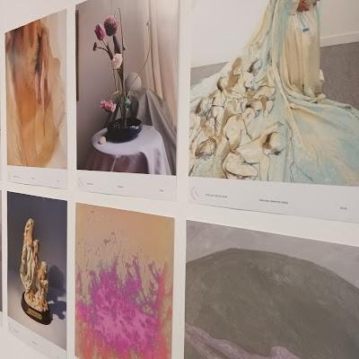 Six art posters are shown on a wall.
Three are abstract, one shows a bouquet of bending pink and white flowers, one shows a woman in a wedding gown upon which clamouring babies and a pregnant belly are painted, and one poster shows a figurative sculpture that is too distorted by the angle of the image to identify.