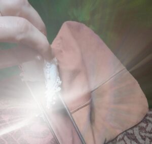 A hand is pulling a dainty white handkerchief out of a faded pink-brown purse with a metal clasp. A huge flash of sunlight reflects off the metal clasp.