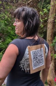 Artist Emily van Lidth de Jeude wearing a black t-shirt with wings on the back, and with a large QR code pinned to the back of her shirt. The QR code leads to a webpage that explains the (dis)robe: Hospital Gown project.