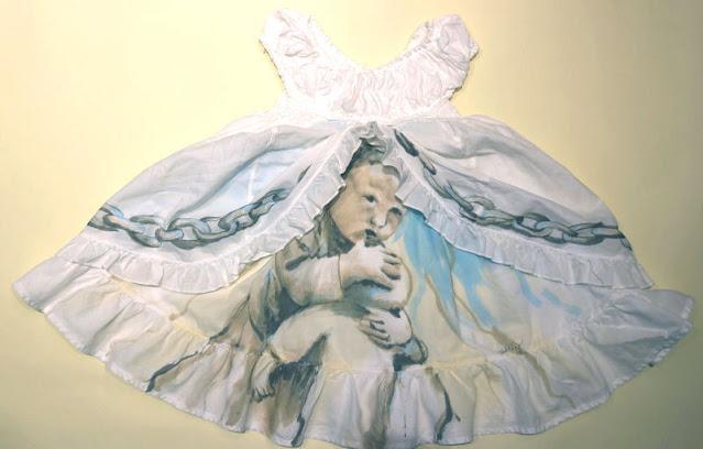 A tiny white child's Christening dress is laid out on a pale yellow background. The dress has ruffles with a chain painted onto them, and from underneath, a baby peeks out, holding a doll to its chest in a protective way.