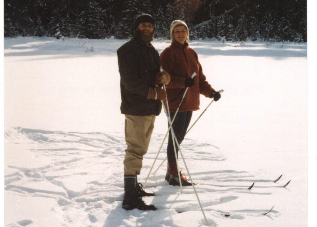 A man and a woman in winter clothing and hats, standing in cross-country skis on a snow-covered frozen lake.