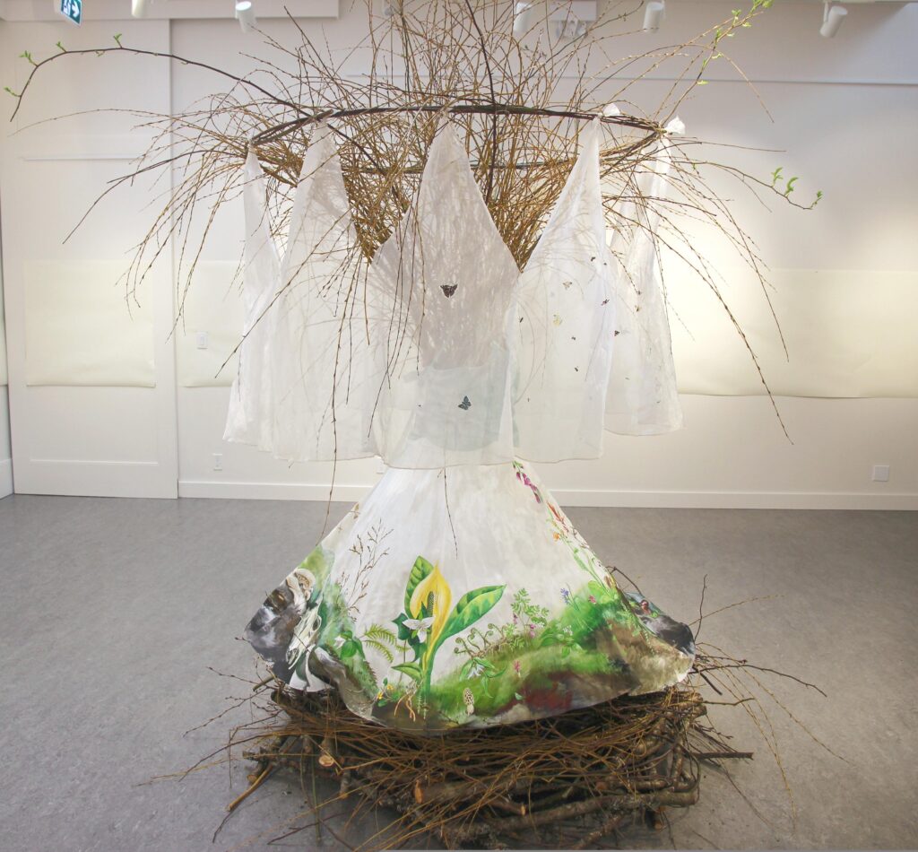In the centre of a gallery is a white dress painted with plants and invertebrates of all seasons, and a circular veil, covered with flying insects, also according to season. The dress is displayed on a giant nest of sticks, with a huge bouquet of willow branches, extending out the top. The branches will leaf out during the exhibition.