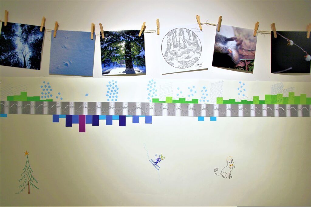 A close-up view of just three weeks of the One Solar Year graph, showing January: daily and nightly temperatures falling below freezing, lunar, solar and tidal cycles, and weather observations including rain and snow. Above the graph are five photos hung by clothespins from a jute string, depicting snowy scenes, a dead rodent, and snowberries. There is also a drawing of a Douglas fir tree trunk. Under the graph are drawings of a Christmas tree, a skier, and a cat.