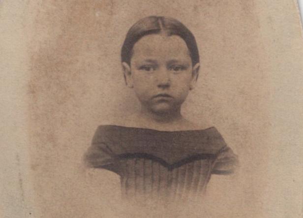 My great great grandmother, Isabella Low Post, around 1863. She's wearing a tailored child's dress, and her straight brown hair is pulled back from her face. She is looking downwards to her right, her mouth closed in a sullen frown. It's a posed portrait, with much fading and brown staining over the child and the white background.